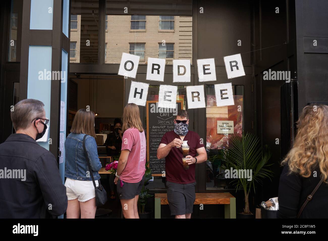 Ein Mann im Gesicht Schal bringt seinen Kaffee auf die Outdoor-Sitzecke im Bijou Cafe in der Innenstadt von Portland, Oregon, am Samstag, 11. Juli 2020. Stockfoto