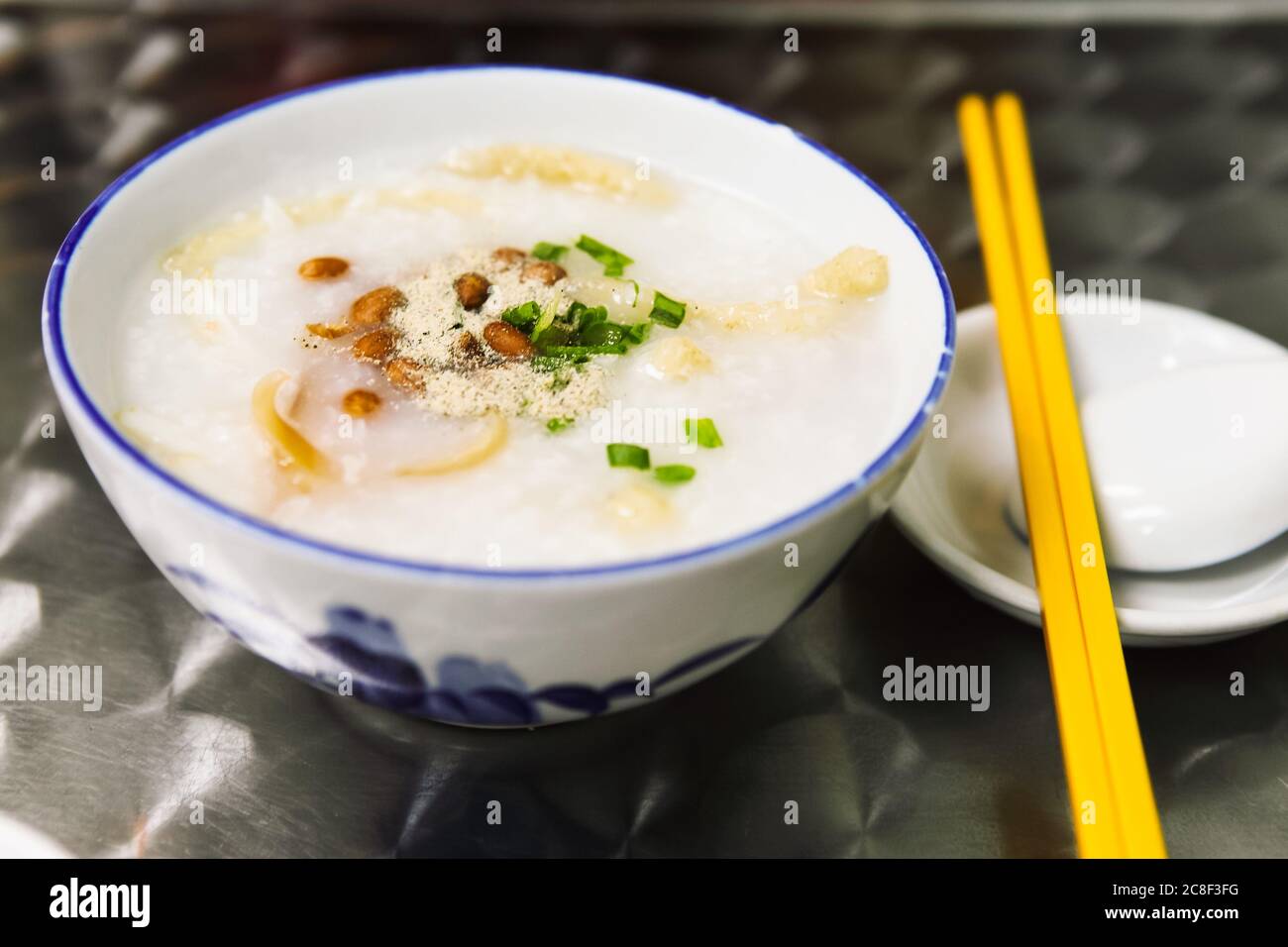 Chinesischer Haferbrei, der mit Pfeffer, Erdnüssen und Frühlingszwiebeln bestreut wird, einige Tintenfische sind darin. Stockfoto