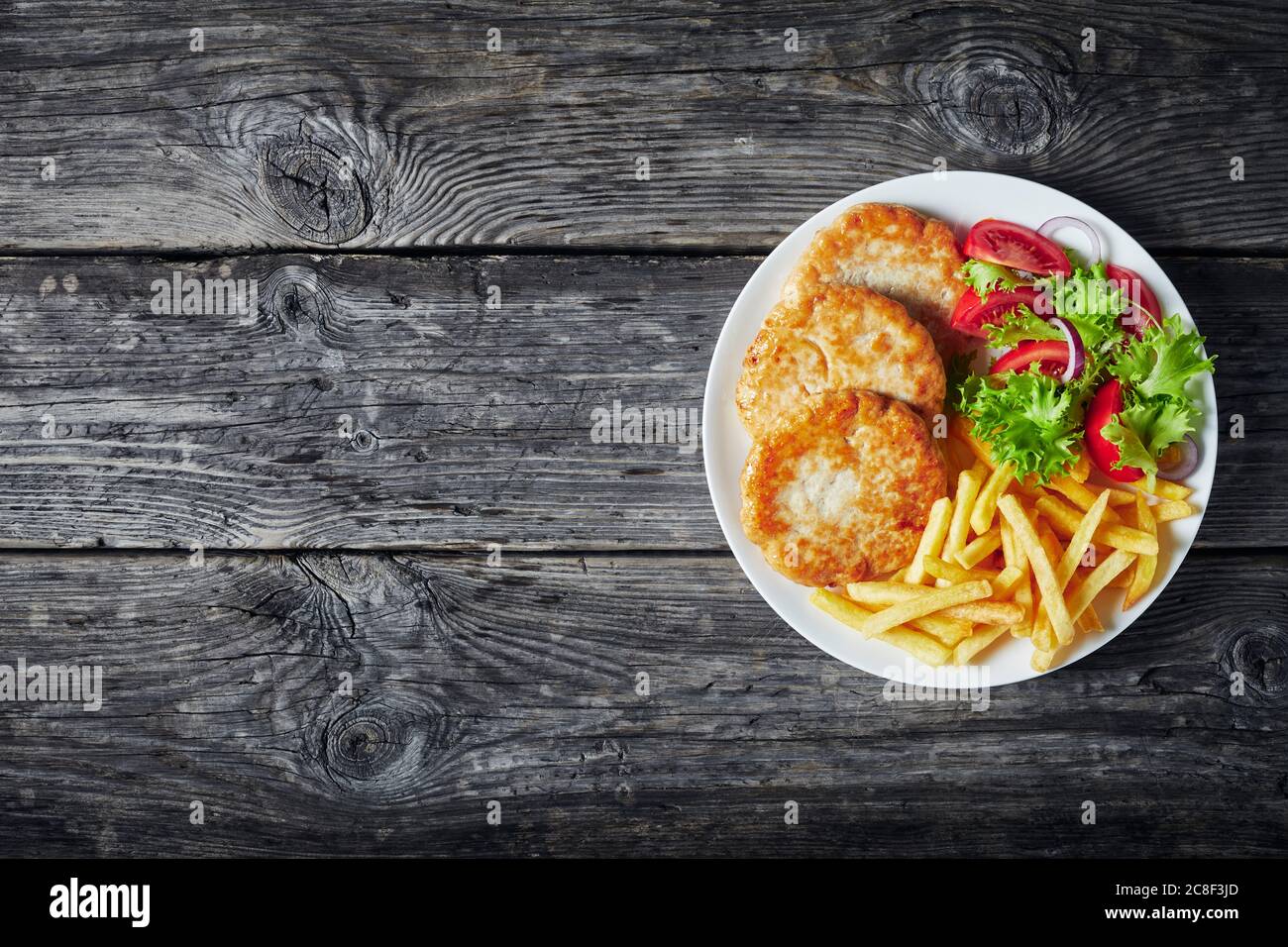 Türkei Burger gebraten serviert mit Salat Tomate Salat und Pommes frites auf einem weißen Teller auf einem rustikalen Holztisch, horizontale Ansicht von oben, flatlay, Stockfoto