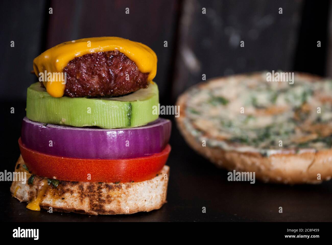 Avocado Burger mit roter Zwiebelscheibe, Burger Bun und Tomate auf einem Holzhintergrund Stockfoto