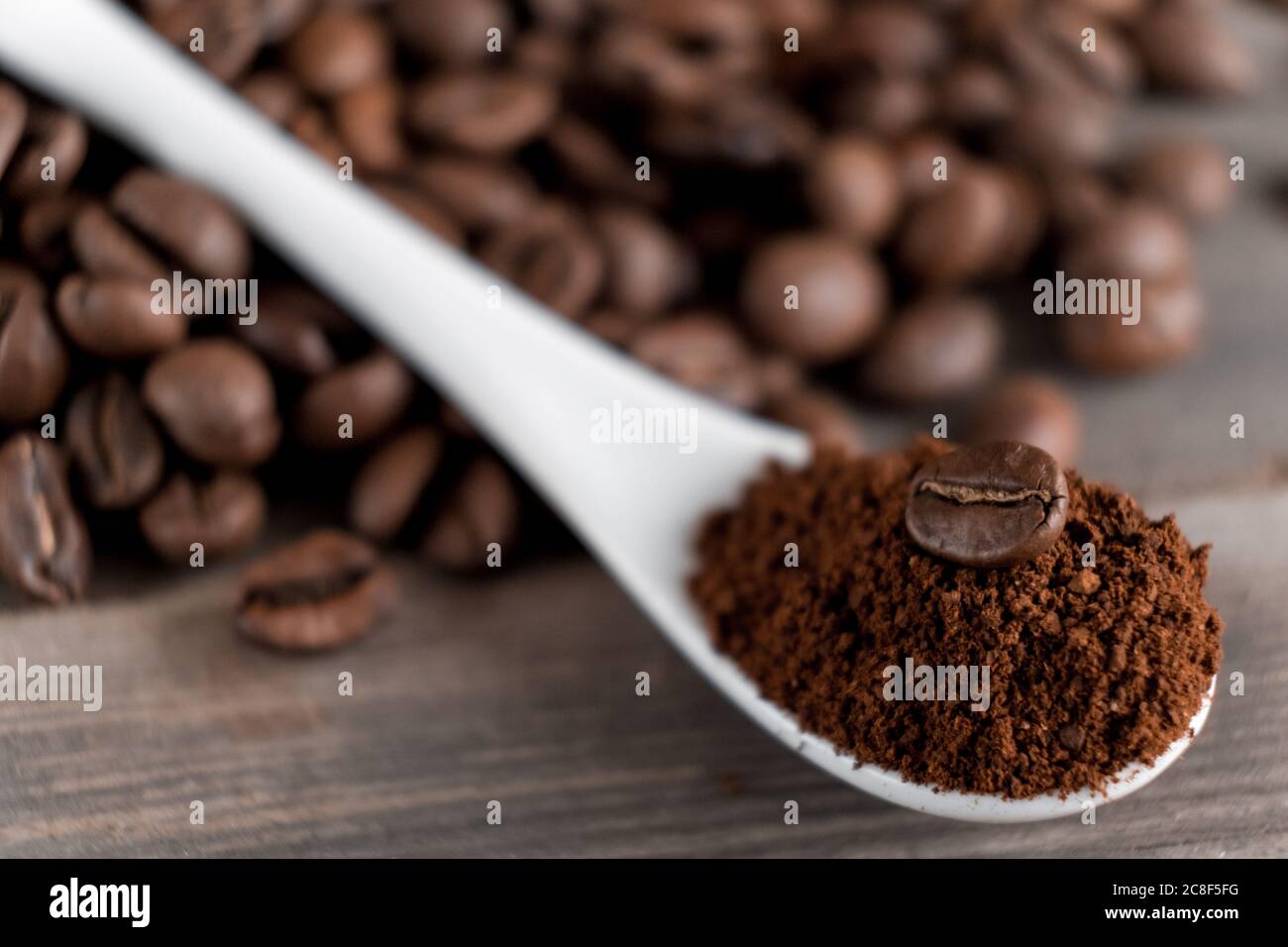Weißer Keramiklöffel mit gemahlenem Kaffee auf Holzgrund gebratene Arabica-Körner. Stockfoto