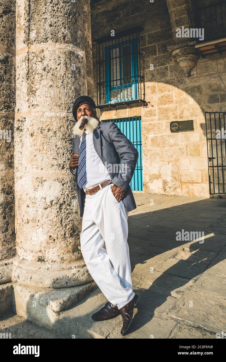 Havanna / Kuba - 04.16.2015: Afro kubaner alter Mann mit einem langen weißen Bart, Anzug und schwarzer Militärmütze, raucht eine große Zigarre Stockfoto
