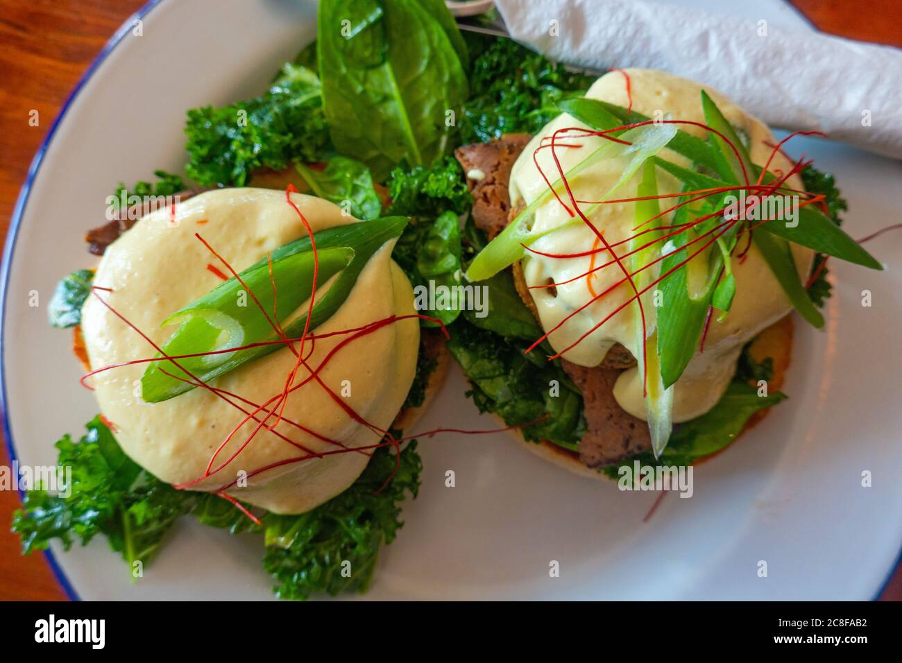 Ein veganes benedict-Frühstück: In einem Restaurant mit Pflanzenbasis werden Fleisch, Haschebraun und Sauce Hollandaise auf Grünkohl und einem englischen Muffin serviert Stockfoto
