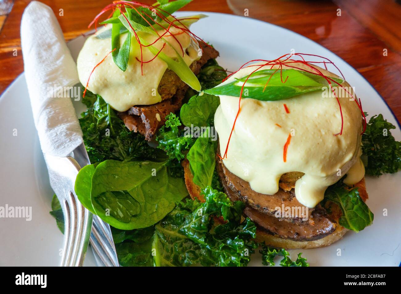 Ein veganes benedict-Frühstück: In einem Restaurant mit Pflanzenbasis werden Fleisch, Haschebraun und Sauce Hollandaise auf Grünkohl und einem englischen Muffin serviert Stockfoto