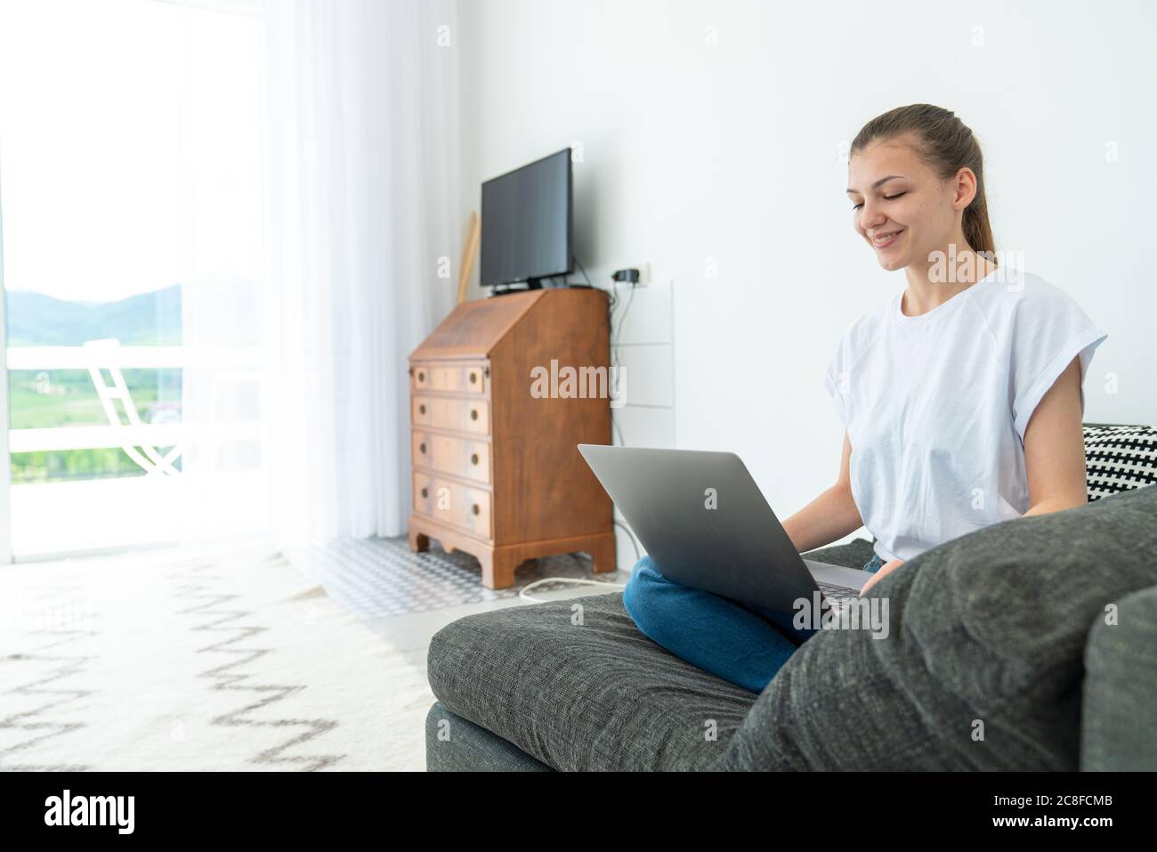 Lächelnd attraktive junge Frau sitzt auf dem Sofa mit Laptop kommunizieren Online-Arbeit zu Hause, glücklich teen Mädchen am Computer tippen Stockfoto