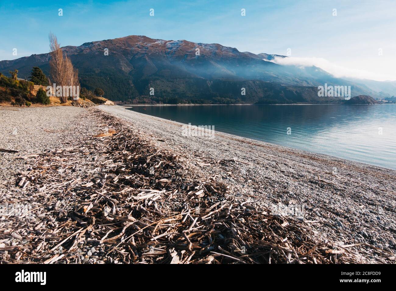 Ein ruhiger, klarer sonniger Wintertag am Scotts Beach, Lake Hawea auf der Südinsel Neuseelands. Ein Bauernbrand wirft eine Rauchschicht über die Bucht Stockfoto