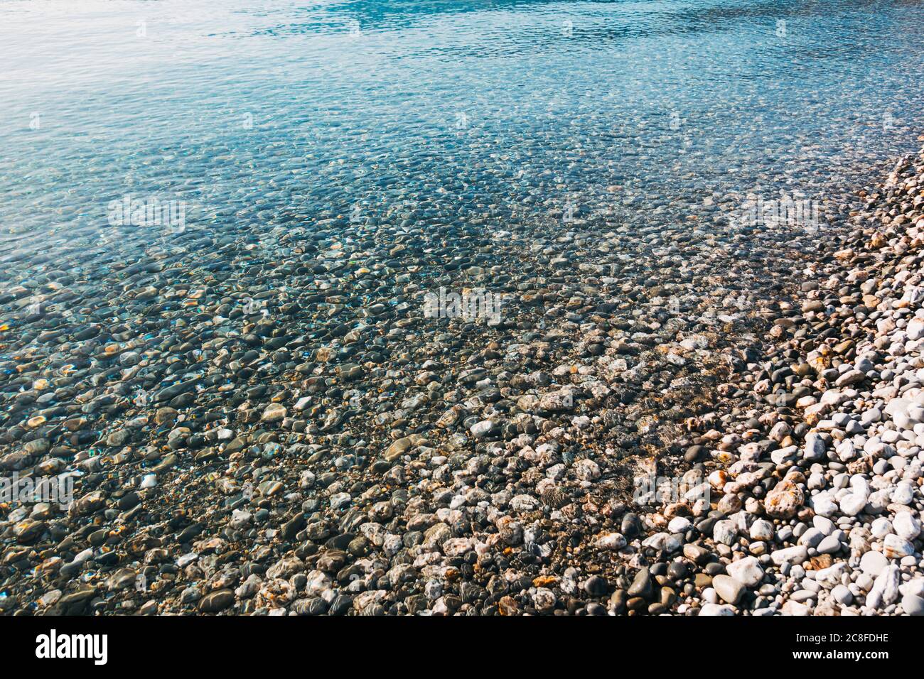 Kristallklares Wasser bricht Licht auf, während es über Kieselsteinen am Ufer und am Seeufer des Lake Hawea, Neuseeland, wäscht Stockfoto