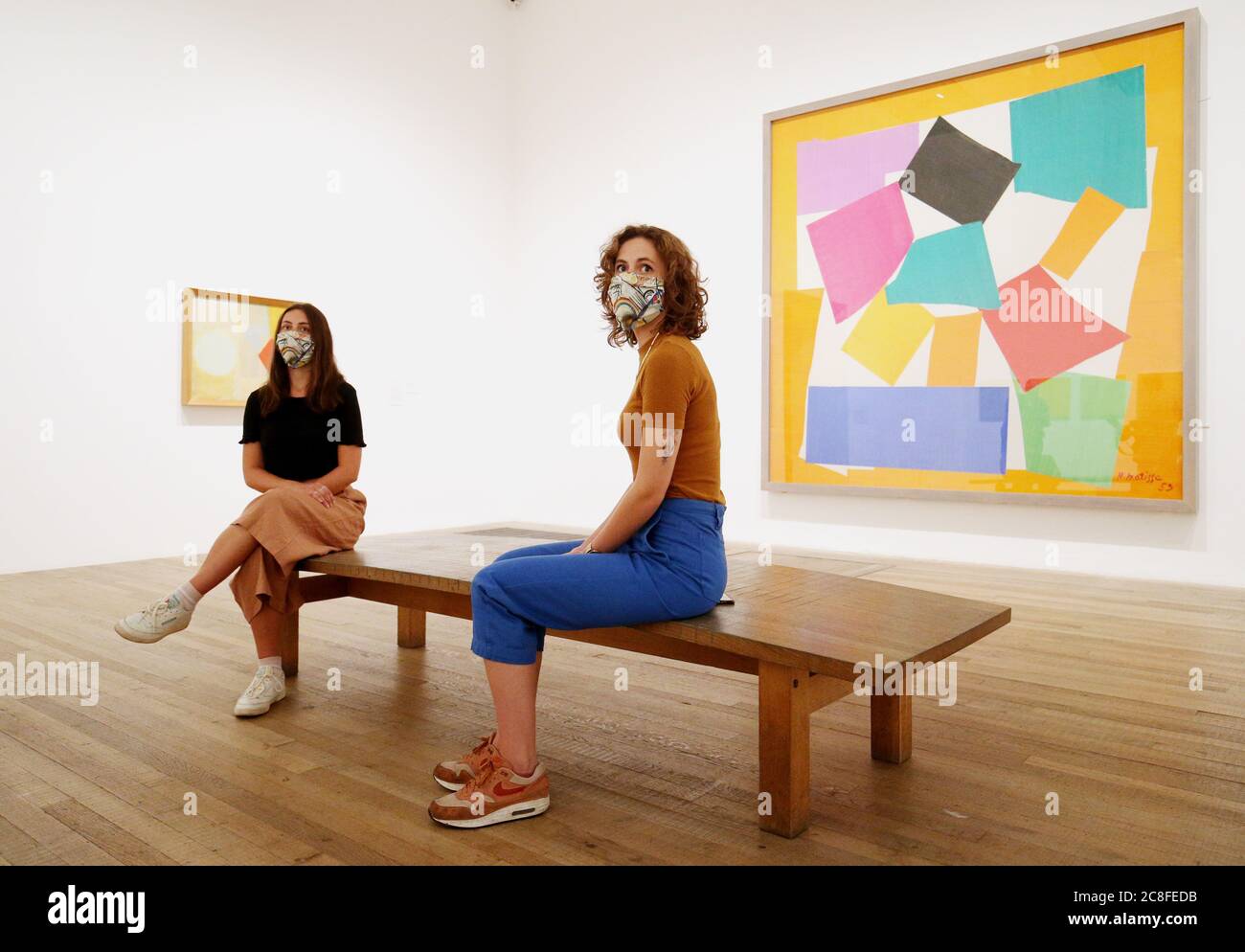 Die Mitarbeiter tragen kunstkunstkunstvolle Masken, während sie auf einer Bank in einer Galerie mit Matisses "die Schnecke" (rechts) in der Tate Modern sitzen, während die Galerie sich darauf vorbereitet, am Montag, den 27. Juli nach der Sperrung des Coronavirus wieder für die Öffentlichkeit zugänglich zu machen. Stockfoto