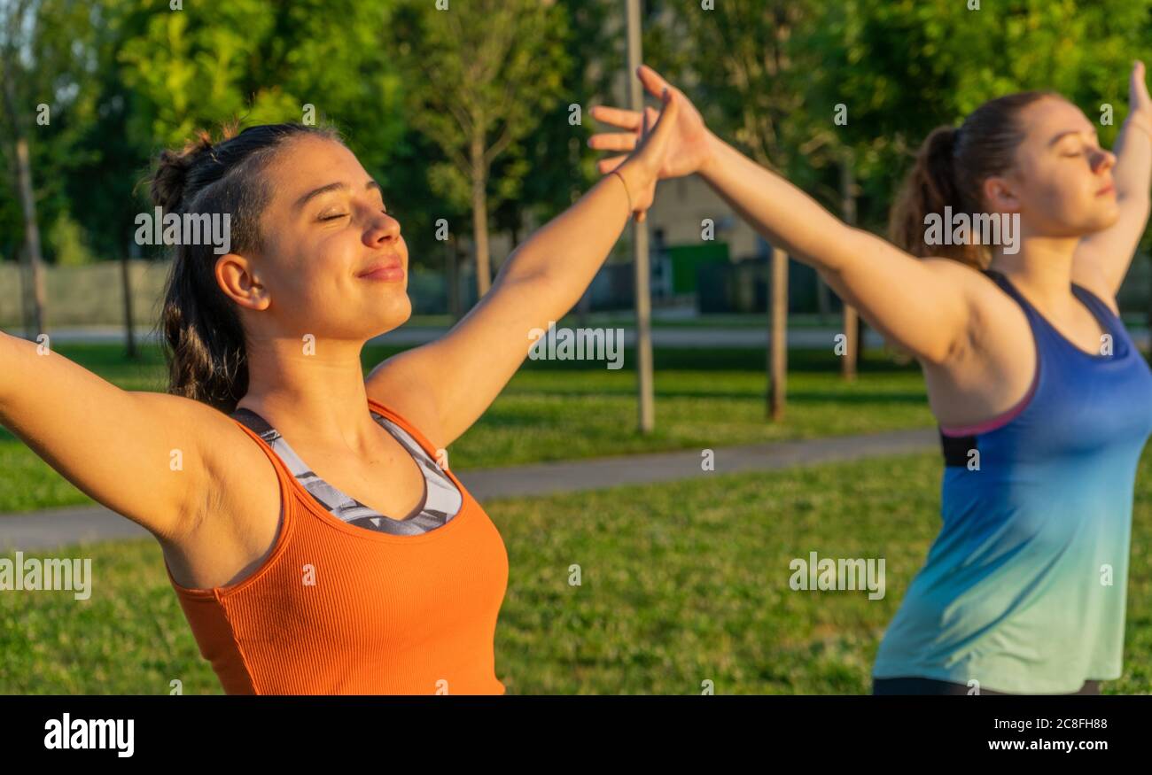 Kaukasische junge Frauen praktizieren Yoga mit geschlossenen Augen Die Sonne im Park Stockfoto