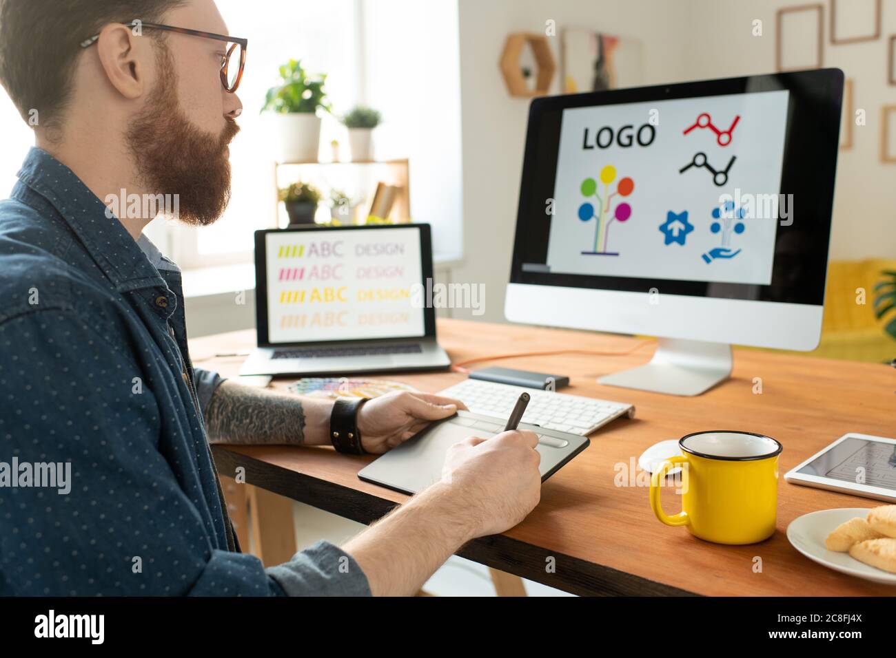 Über der Schulter Blick auf gebärtete Designer in Brille sitzen am Schreibtisch und mit Zeichenblock während der Arbeit an Website-Grafiken Stockfoto