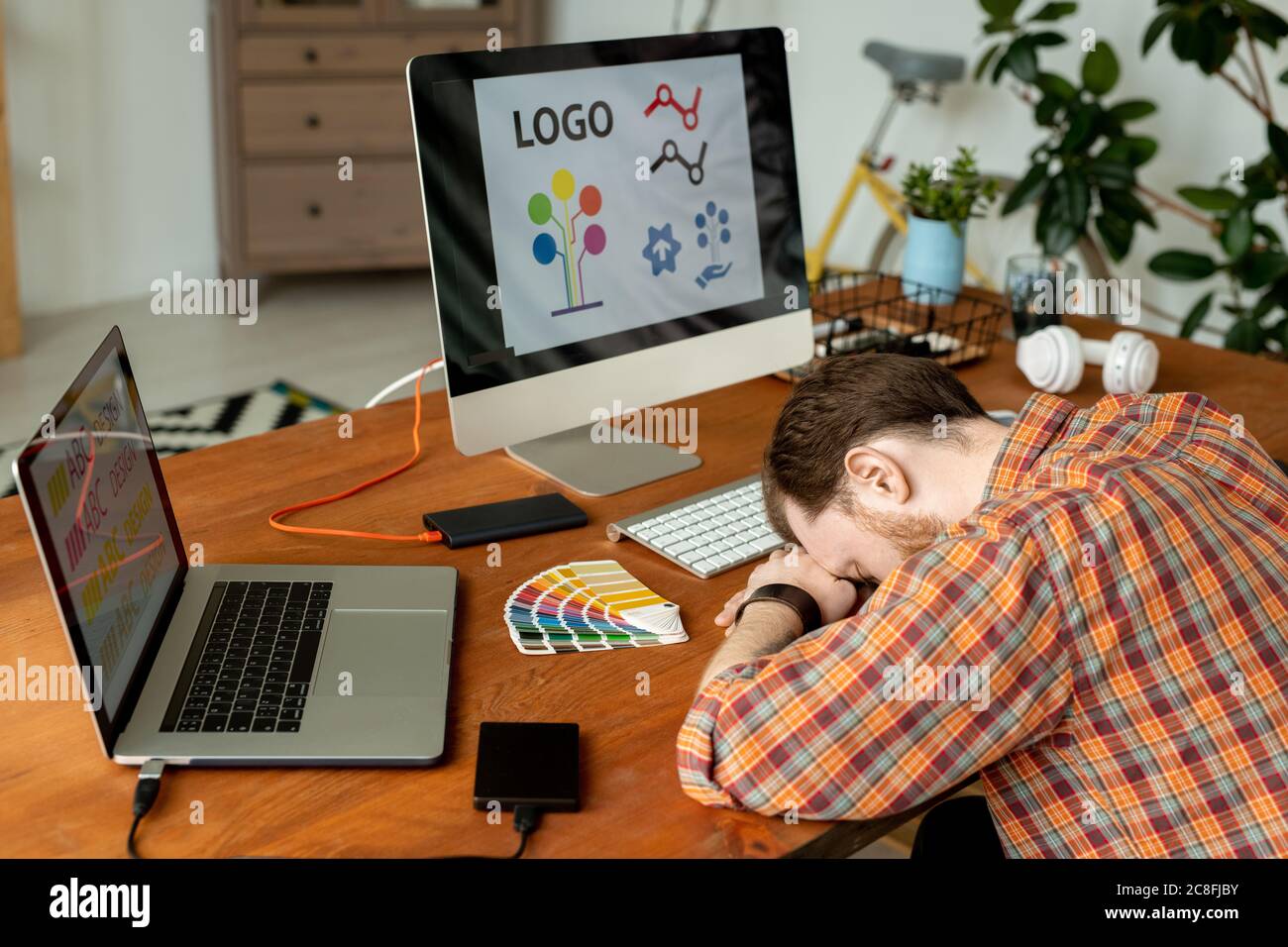 Überarbeiteter Designer schläft am Arbeitsplatz mit modernen Computern und Festplatten Stockfoto