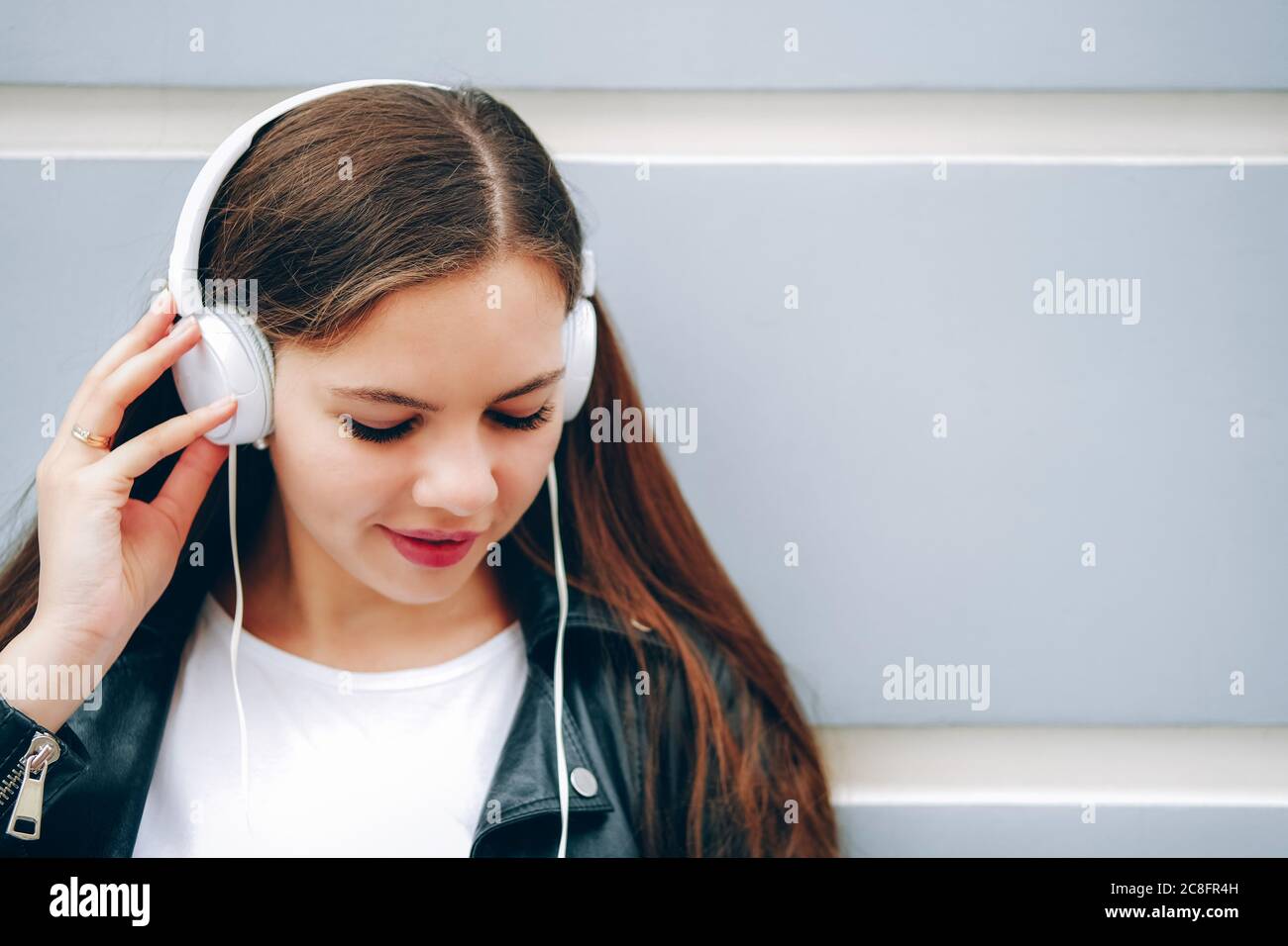 Junge Frau mit langen Haaren, die draußen Musik in weißen Kopfhörern hört. Mädchen in der Stadt. Leerzeichen für Text. Stockfoto