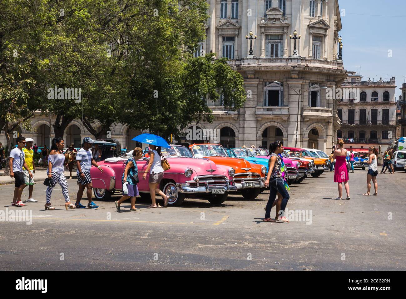 Havanna / Kuba - 04.15.2015: Touristen und Einheimische, die vor bunten klassischen amerikanischen Autos laufen, die als Touristentaxis in Kuba benutzt werden Stockfoto