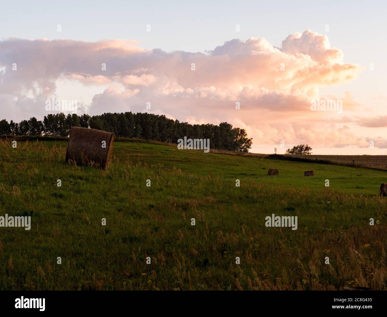 Sonnenuntergang Sonnenaufgang auf einem Getreidefeld auf der Insel Rügen mit einer Farm, Bäumen, Strohballen, roten Mohnblumen nach einem Gewitter Stockfoto