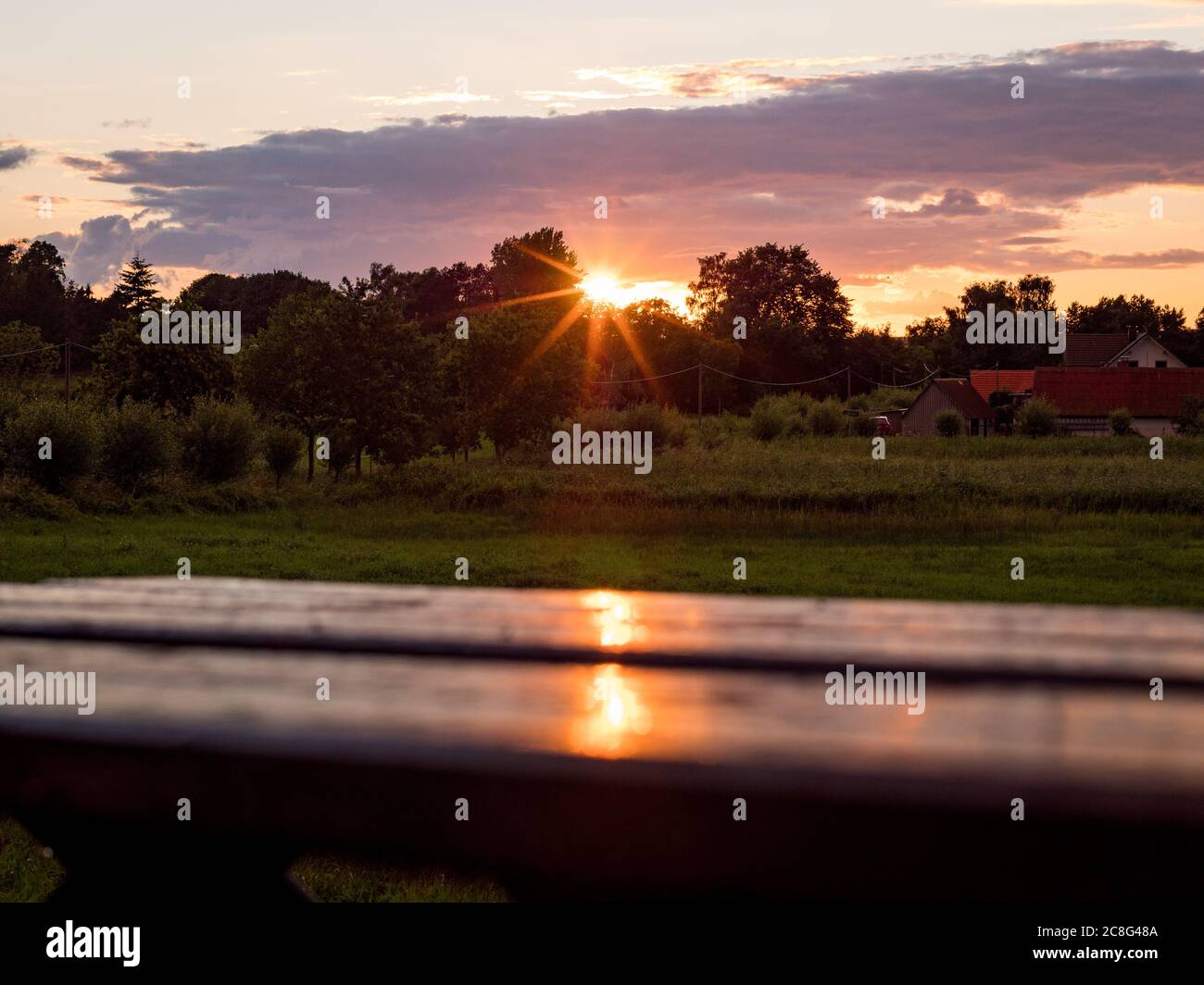 Sonnenuntergang Sonnenaufgang auf einem Getreidefeld auf der Insel Rügen mit einer Farm, Bäumen, Strohballen, roten Mohnblumen nach einem Gewitter Stockfoto