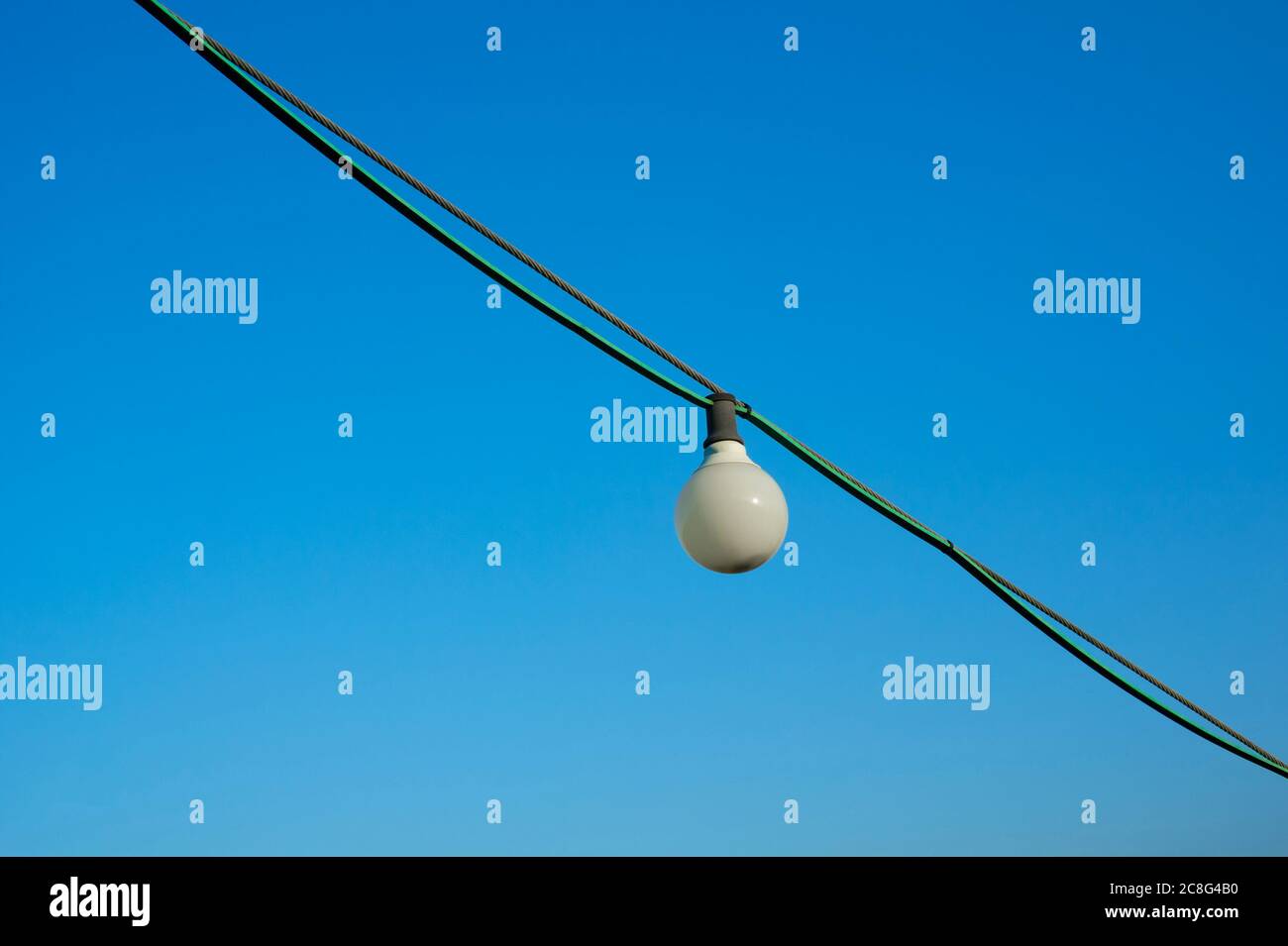 Weiße Glühlampe auf Draht. Im Hintergrund ein klarer blauer Himmel. Die Glühlampe ist bei Tageslicht ausgeschaltet. Minimalistische Komposition mit großem Kopierraum Stockfoto