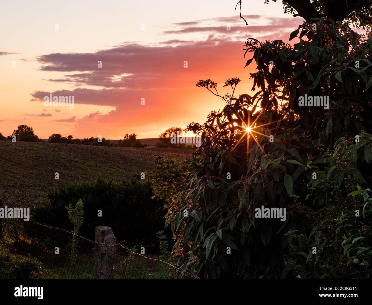 Sonnenuntergang Sonnenaufgang auf einem Getreidefeld auf der Insel Rügen mit einer Farm, Bäumen, Strohballen, roten Mohnblumen nach einem Gewitter Stockfoto