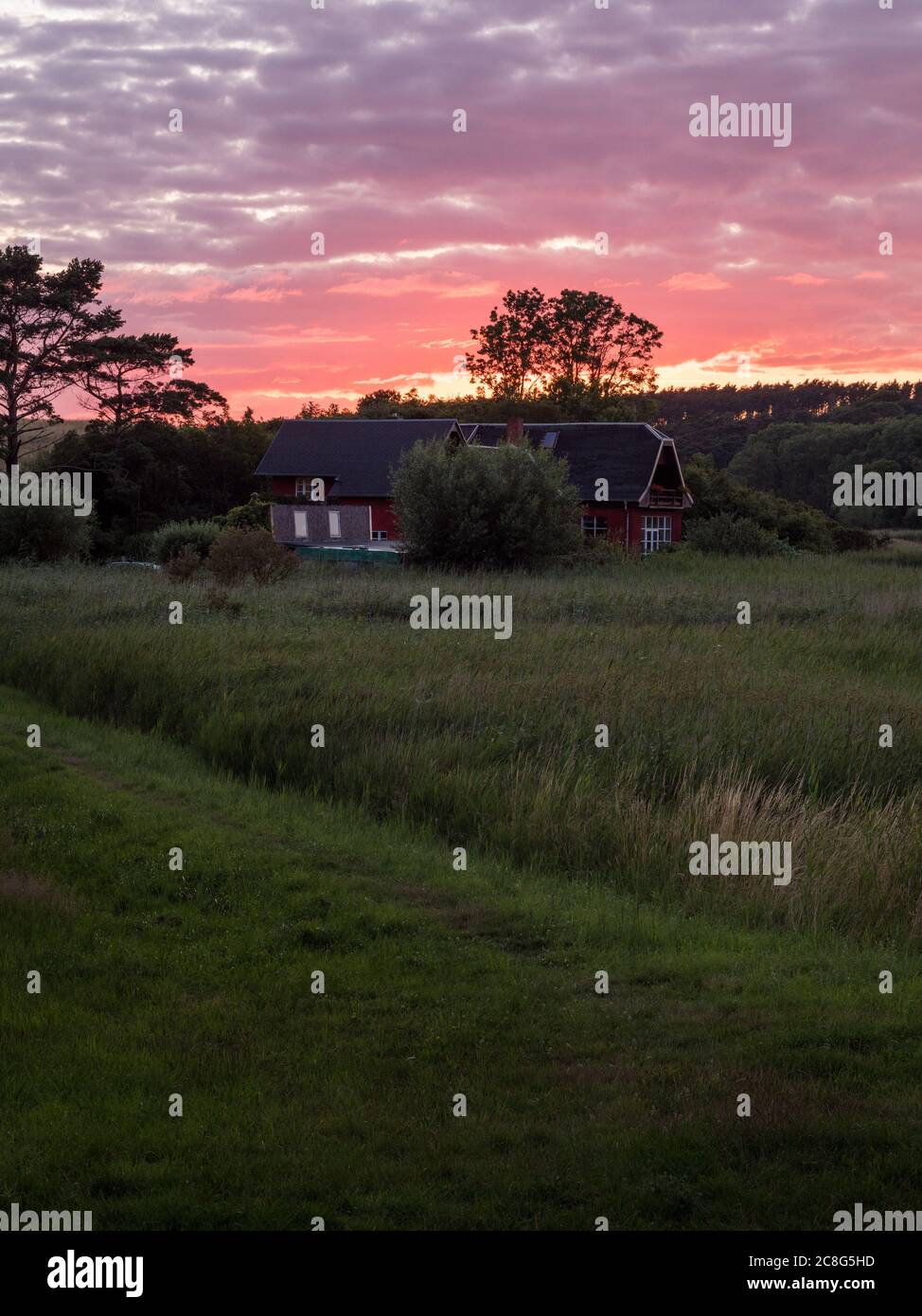 Sonnenuntergang Sonnenaufgang auf einem Getreidefeld auf der Insel Rügen mit einer Farm, Bäumen, Strohballen, roten Mohnblumen nach einem Gewitter Stockfoto