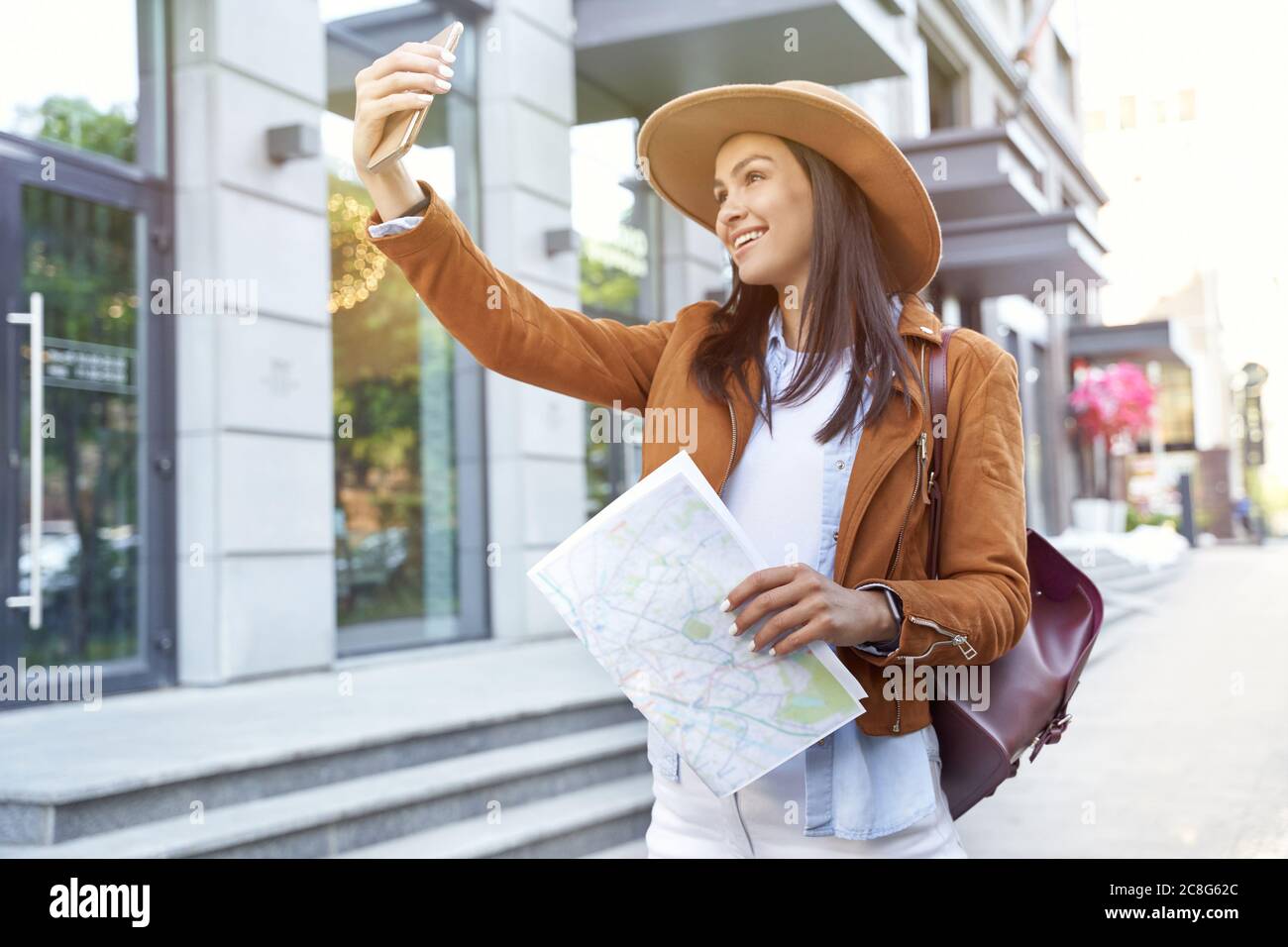 Reisen in Europa. Junge glückliche weibliche Reisende oder Touristen tragen Hut und Rucksack halten Karte, machen Selfie, während auf der Stadt Straße stehen. Positive Emotionen. Reisen, Tourismus, Urlaub Stockfoto