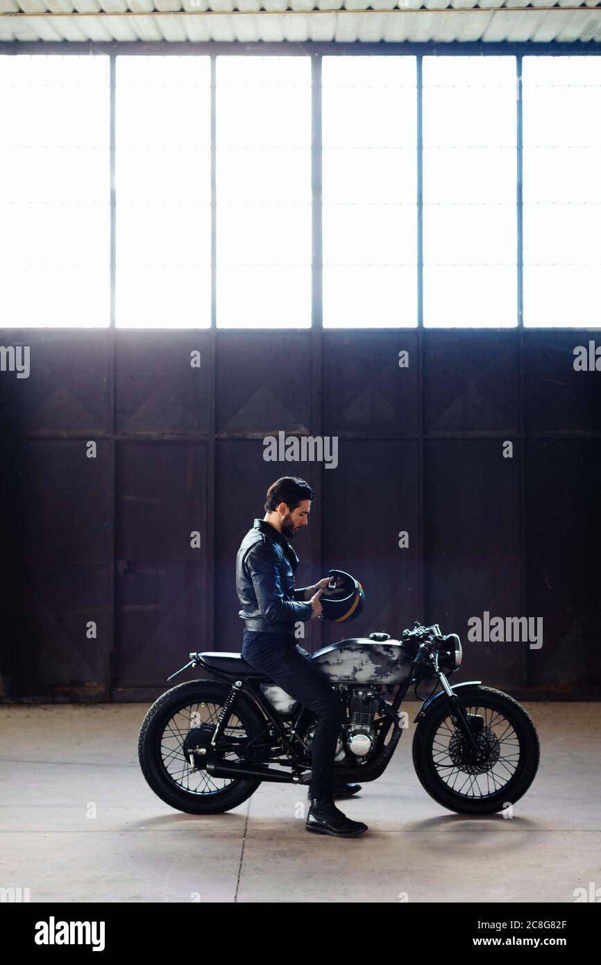 Junge männliche Motorradfahrer gebietsübergreifende Oldtimer Motorrad in leere Lager, volle Länge Stockfoto