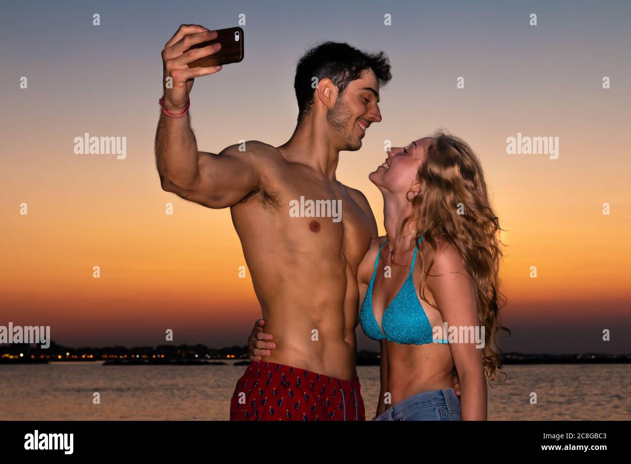 Junges Paar nimmt Selfie im Abendlicht - zwei lächelnde junge Liebhaber machen Selfie am Strand im Sonnenuntergang Stockfoto