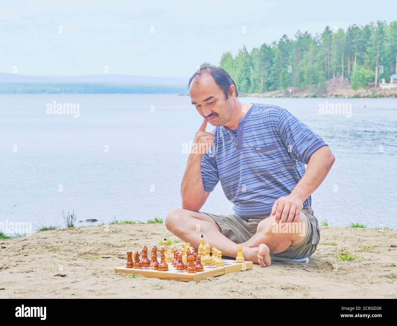 Senior Asian Mann, der einen Zug in einem Schachspiel und sitzt am Strand in der Nähe des Sees. Digitales Detox-Konzept Stockfoto