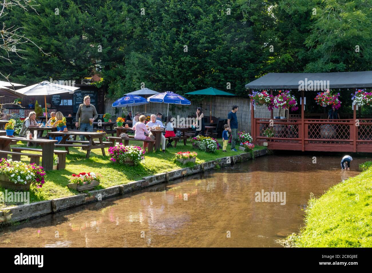 Menschen essen und trinken im Pub Garten des Compasses Inn neben dem Mühlbach in Gomshall Dorf, Surrey, England, Großbritannien, im Sommer Stockfoto