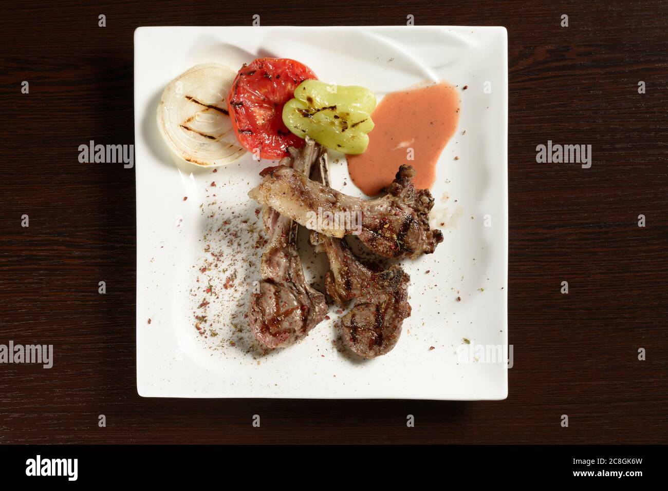 Grillen Sie Rinderrippen mit gegrilltem Gemüse aus Tomaten, Zwiebeln und Paprika auf einem quadratischen Teller auf einem Holztisch. Draufsicht. Fotos für das Restaurant Stockfoto