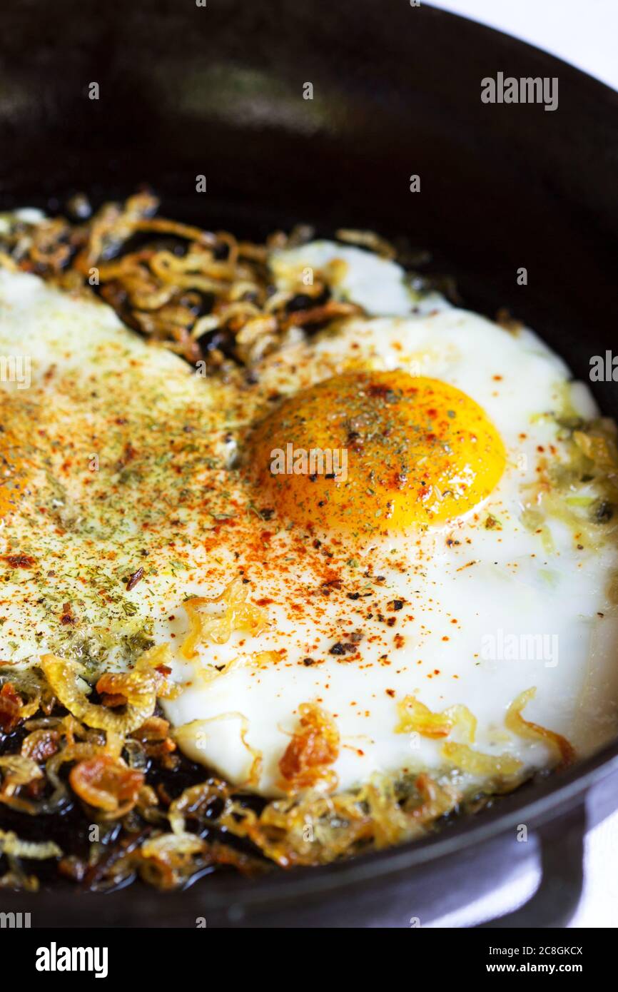 Spiegeleier mit Zwiebeln und Gewürzen in einer gusseisernen Pfanne. Stockfoto