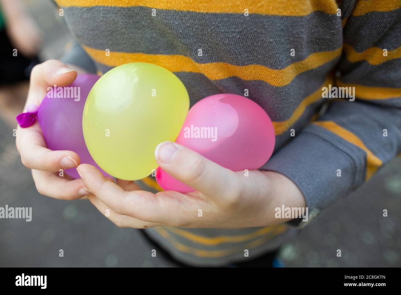Kind trägt gestreiftes Hemd sorgfältig hält Wasser Luftballons in den Händen Stockfoto
