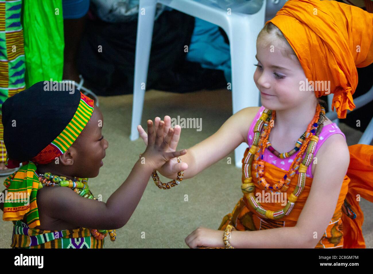 Afrikanische und weiße (kaukasische) Mädchen sitzen zusammen, schauen sich gegenseitig an und berühren die Hände Stockfoto