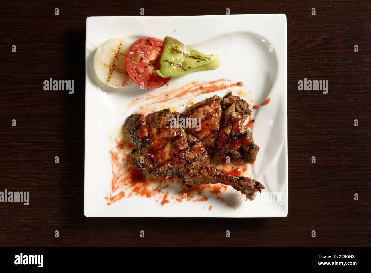 Barbecue Chicken Oberschenkel mit gegrilltem Gemüse von Tomaten, Zwiebeln und Paprika auf einem quadratischen Teller auf einem Holztisch. Draufsicht. Fotos für Restaurant A Stockfoto
