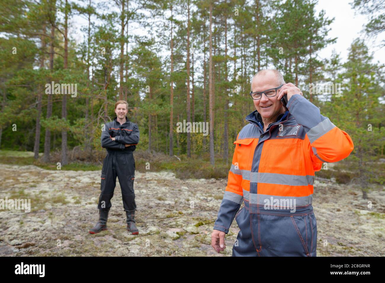 Glücklicher reifer Mann im Wald mit einem Handy im Hintergrund Stockfoto