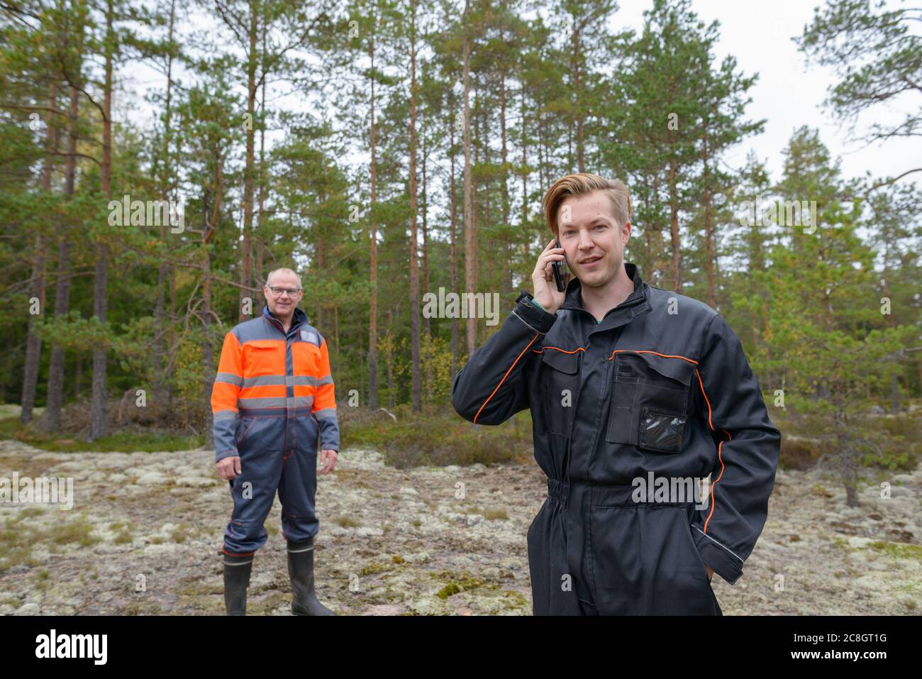 Glücklicher junger Mann im Wald mit einem Handy im Hintergrund Stockfoto