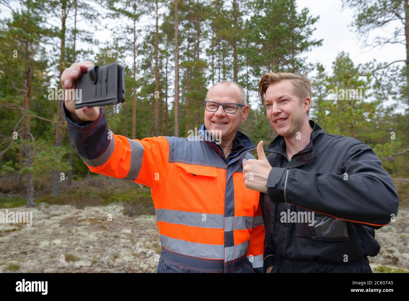 Portrait von glücklichen reifen Mann und jungen Mann zusammen Selfie und Daumen nach oben im Wald Stockfoto