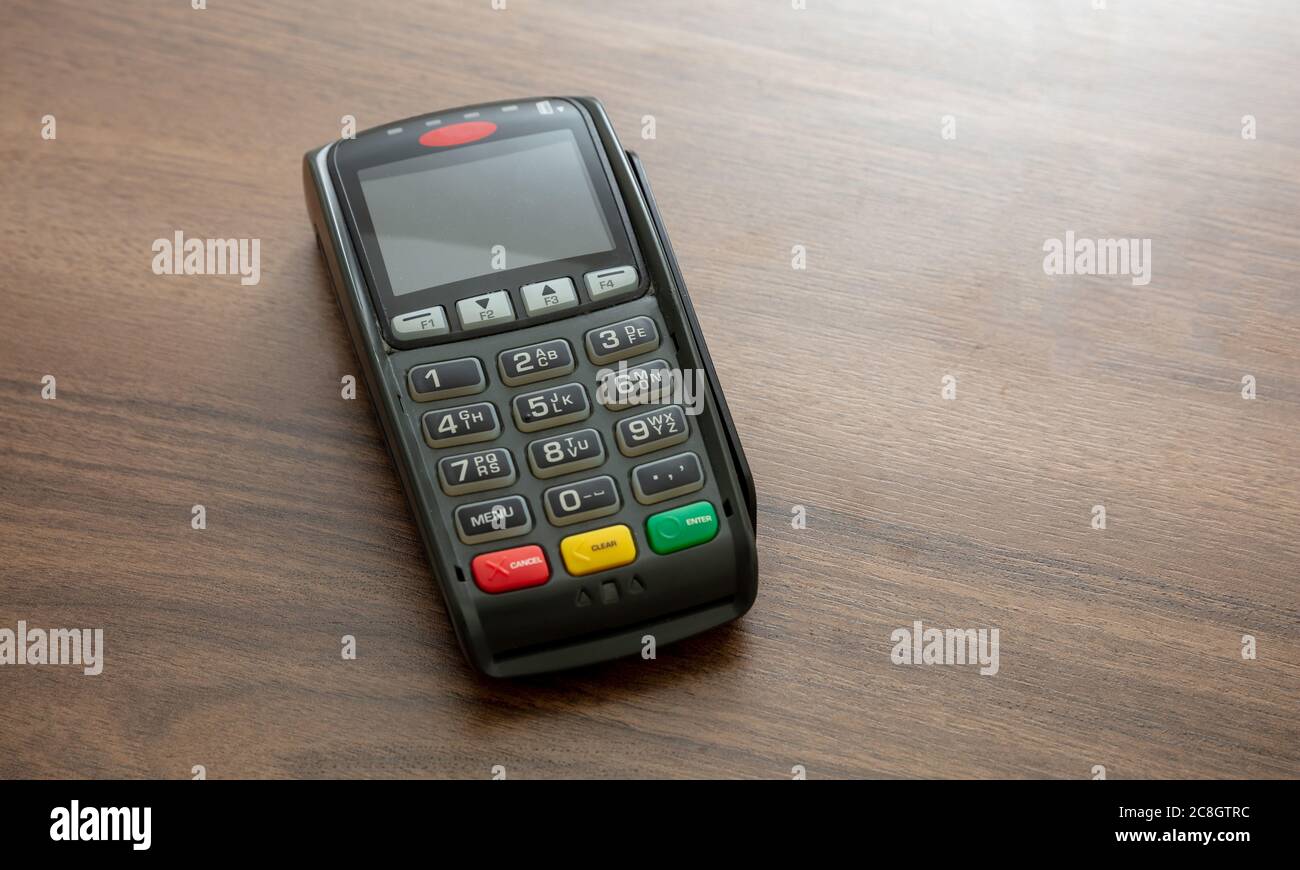 POS-Terminal isoliert auf Holzhintergrund, Kopierraum.Terminal-Kassenautomat für kontaktloses Bezahlen mit Kreditkarte. Bankausstattung, NFC Stockfoto