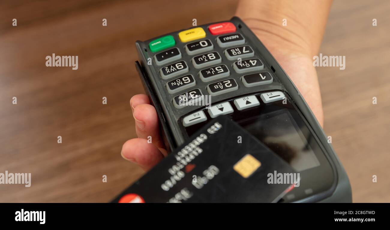 Bezahlung mit NFC-Technologie. Hand hält eine Kreditkarte über einem POS-Terminal, Holztheke Hintergrund, Nahaufnahme Ansicht.Terminal Kasse Maschine fo Stockfoto