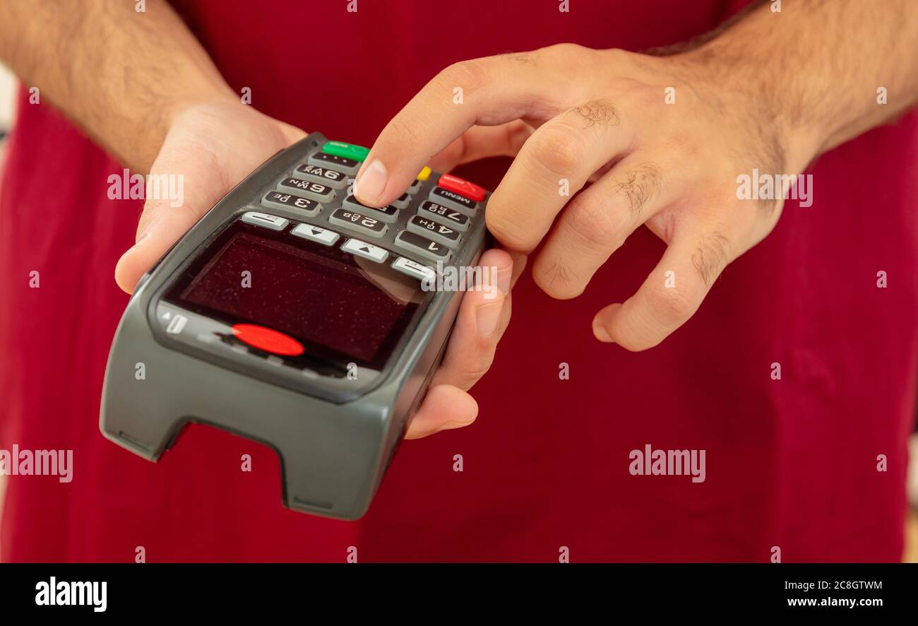 Mann hält eine Zahlung Swipe Maschine und Eingabe, Nahaufnahme. Kreditkartenleser, Kassenterminal-Bezahlkonzept. Stockfoto