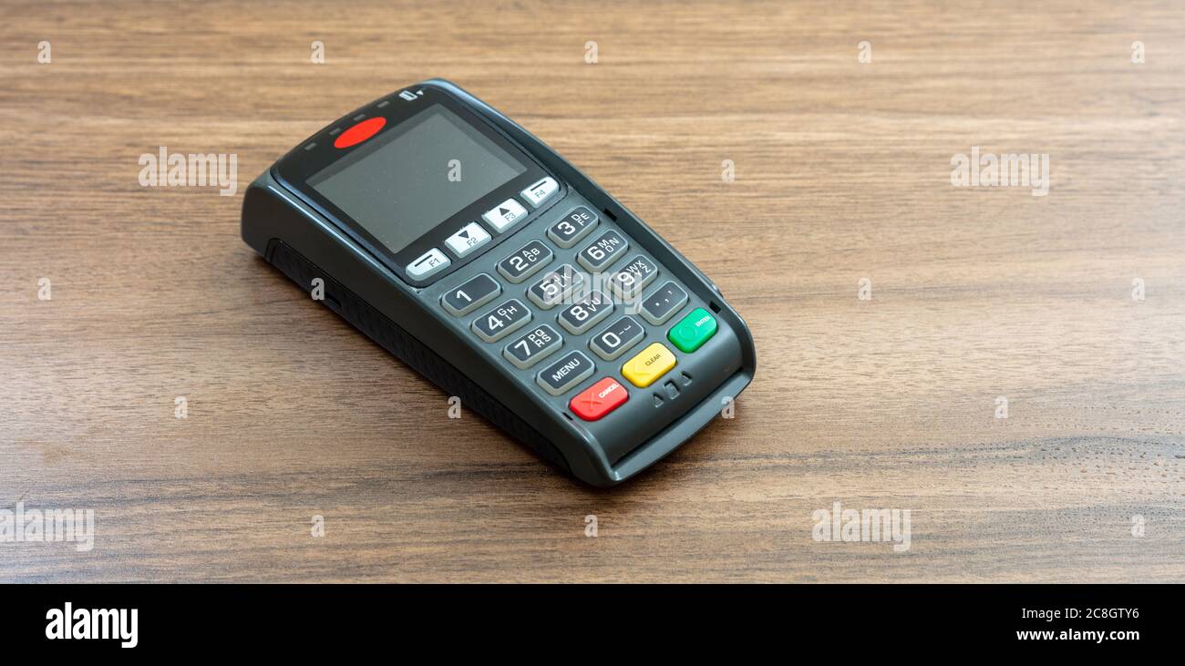 POS-Terminal isoliert auf Holzhintergrund, Kopierraum.Terminal-Kassenautomat für kontaktloses Bezahlen mit Kreditkarte. Bankausstattung, NFC Stockfoto
