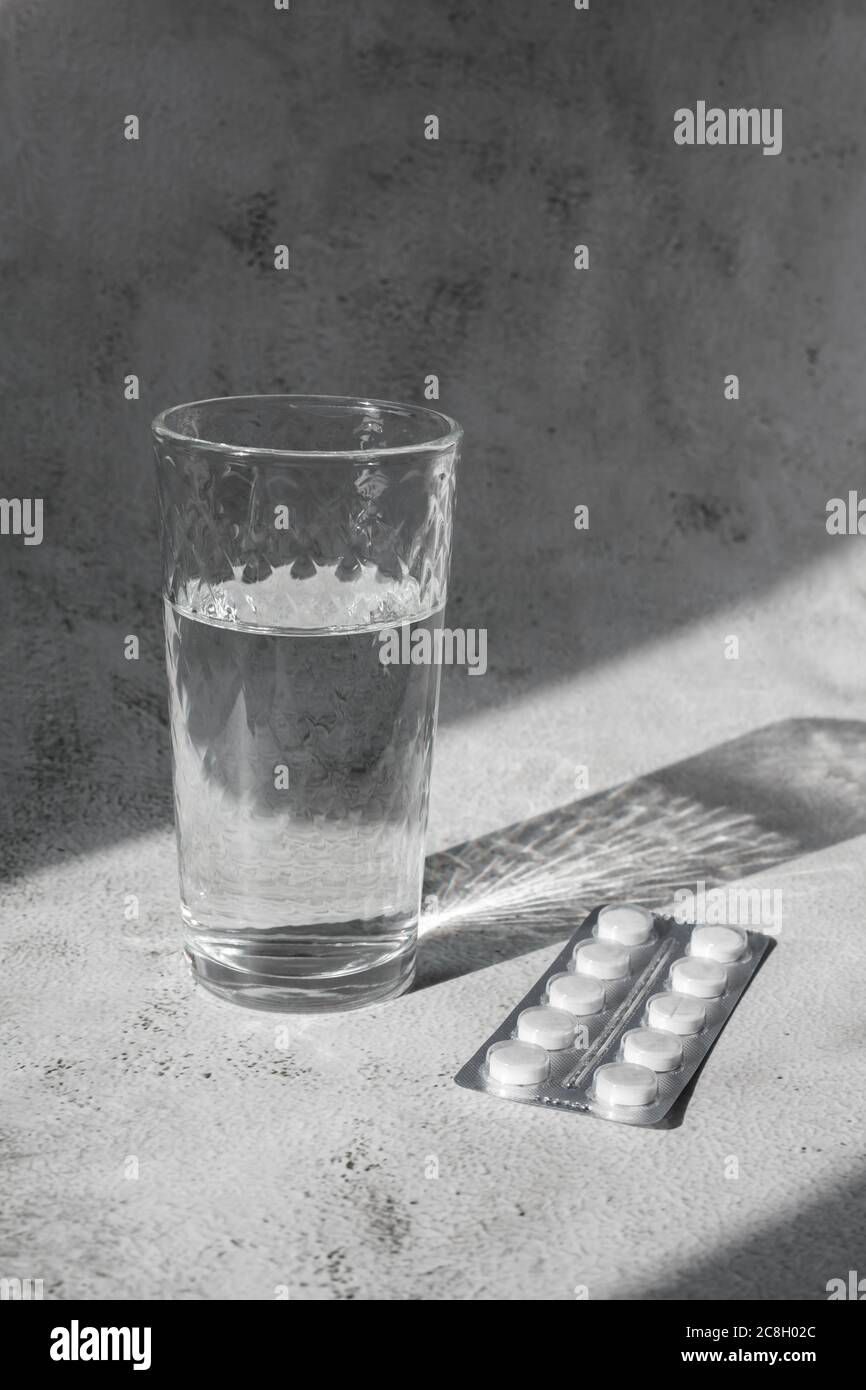 Transparentes Glas Wasser mit weißen Pillen im Kontrastlicht. Kopfschmerz-Konzept Stockfoto