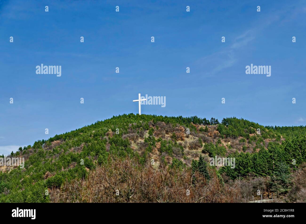 Ein majestätisches Holzkreuz erhebt sich über einem Hügel mit Nadelbäumen und Laubbäumen gegen den blauen Himmel in der Nähe von Blagoevgrad, Bulgarien Stockfoto