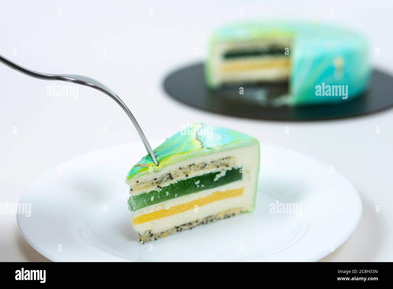 Nahaufnahme Essen Scheibe Mousse Kuchen bedeckt blau und grün Spiegelglasur. Französisches Dessert. Gefrorener Spiegel Sahnehäubchen auf dem Kuchen. Backen und Süßwaren Co Stockfoto