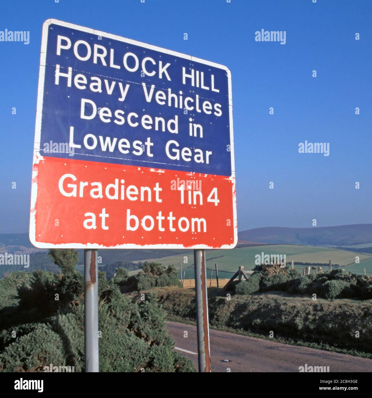 Straßenverkehrswarnschild in Porlock Hill auf A39 steile Steigung instructing Verwendung von niedrigen Gang hügelige Ackerland Landschaft Somerset England Großbritannien Stockfoto