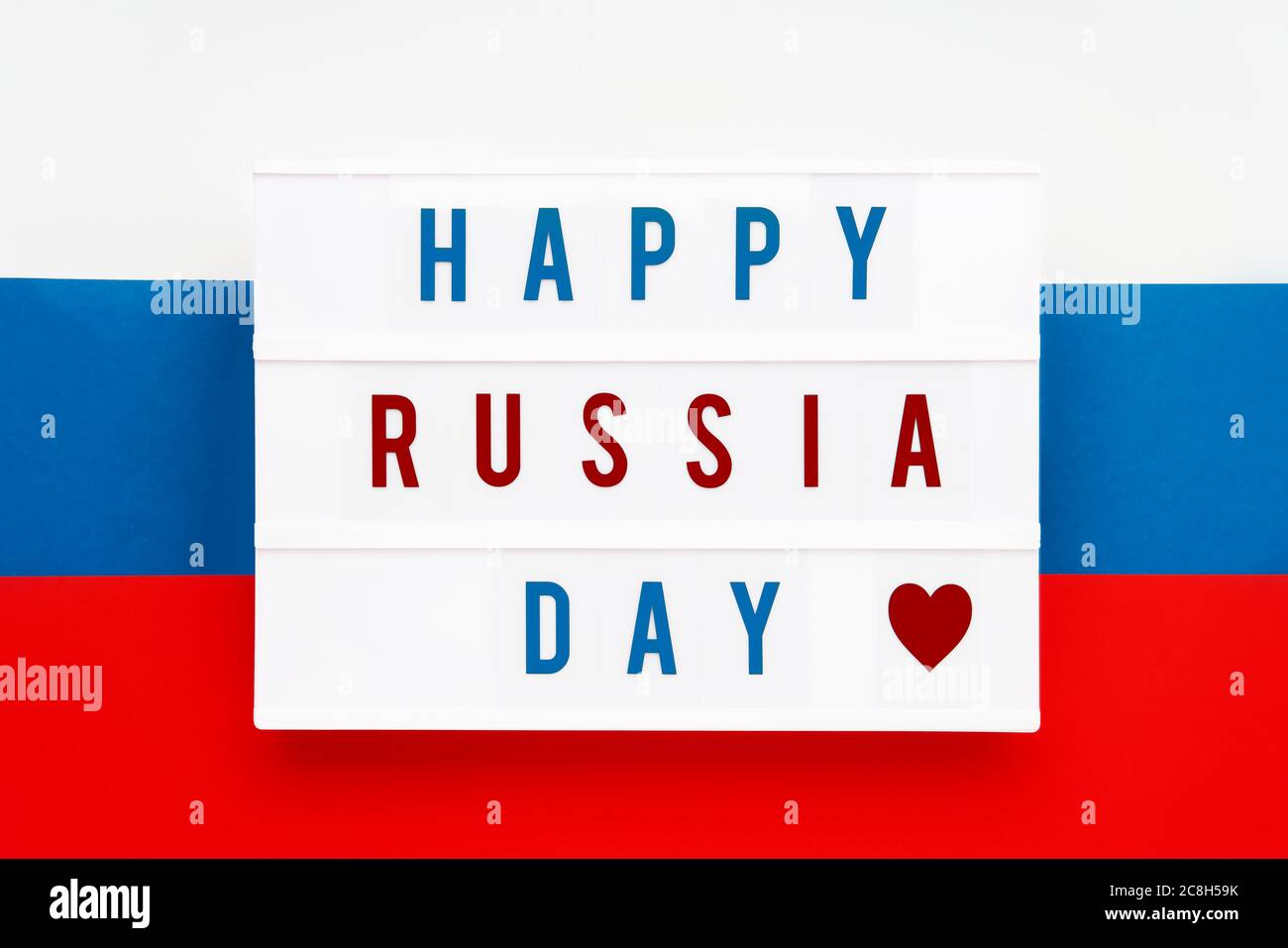 HAPPY RUSSIA DAY in Leuchtkasten auf russische Flagge Hintergrund geschrieben. Datum des Unabhängigkeitstages. Draufsicht. Stockfoto