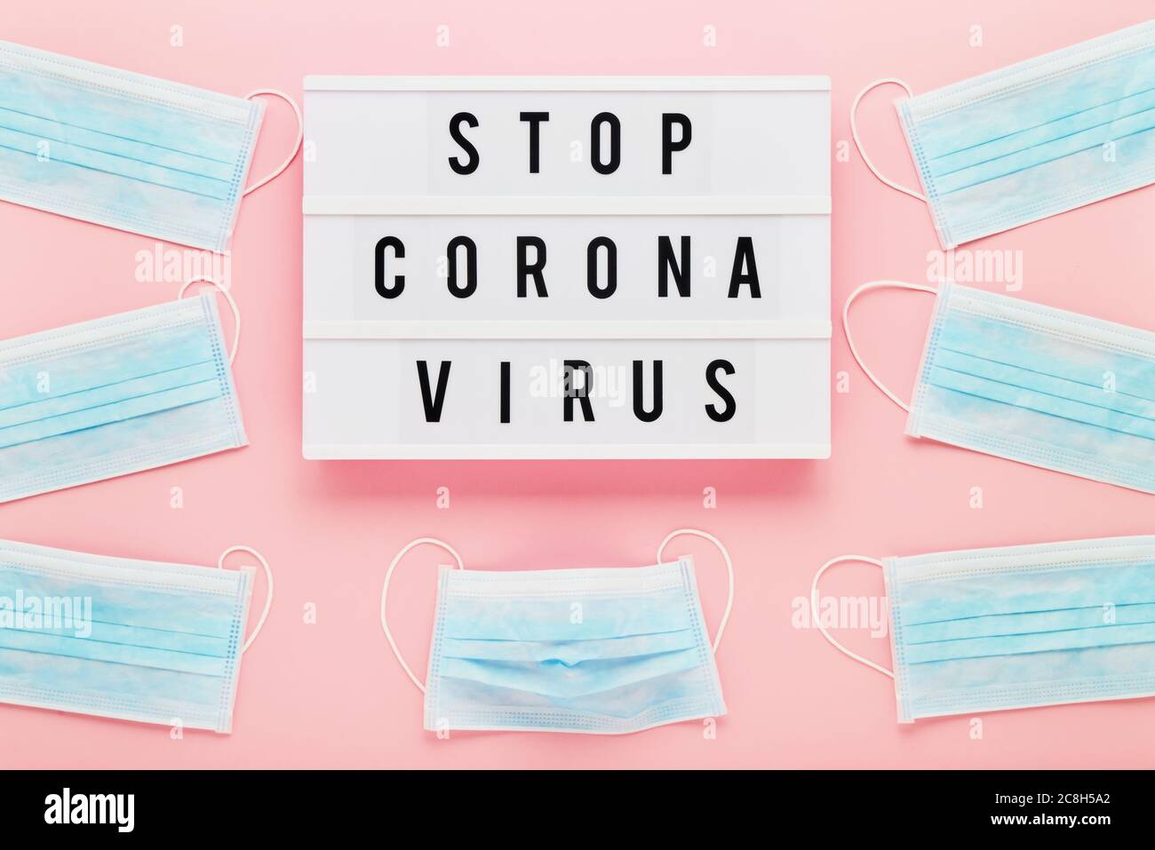STOP CORONA VIRUS in Leuchtkasten und medizinische Schutzmasken auf rosa Hintergrund geschrieben. Draufsicht, Kopierbereich für Text. Stockfoto