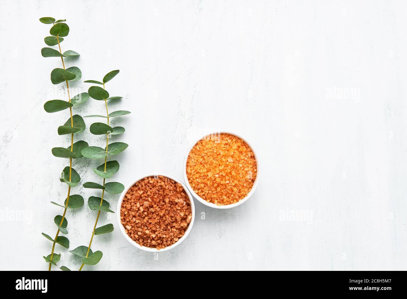 Buntes Badesalz in einer kleinen Schüssel und zwei Eukalyptuszweige auf weißem Grund. Draufsicht, Kopierbereich für Text. SPA- und Gesundheitskonzept. Stockfoto