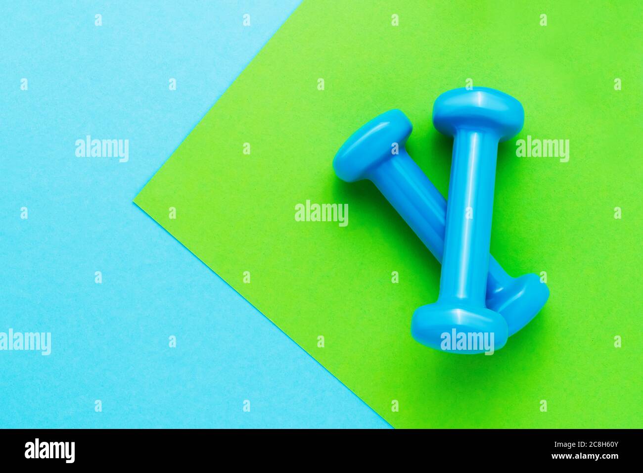 Blaue Kurzhanteln liegen auf grün-blauem Hintergrund. Das Konzept des gesunden Lebensstils. Platz für Text kopieren, Draufsicht Stockfoto