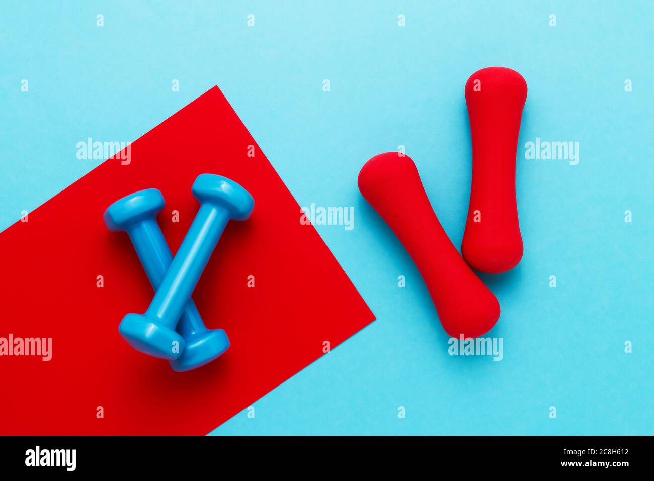 Rote und blaue Hanteln liegen auf rot-blauem Hintergrund. Das Konzept des gesunden Lebensstils. Platz kopieren, Draufsicht. Stockfoto