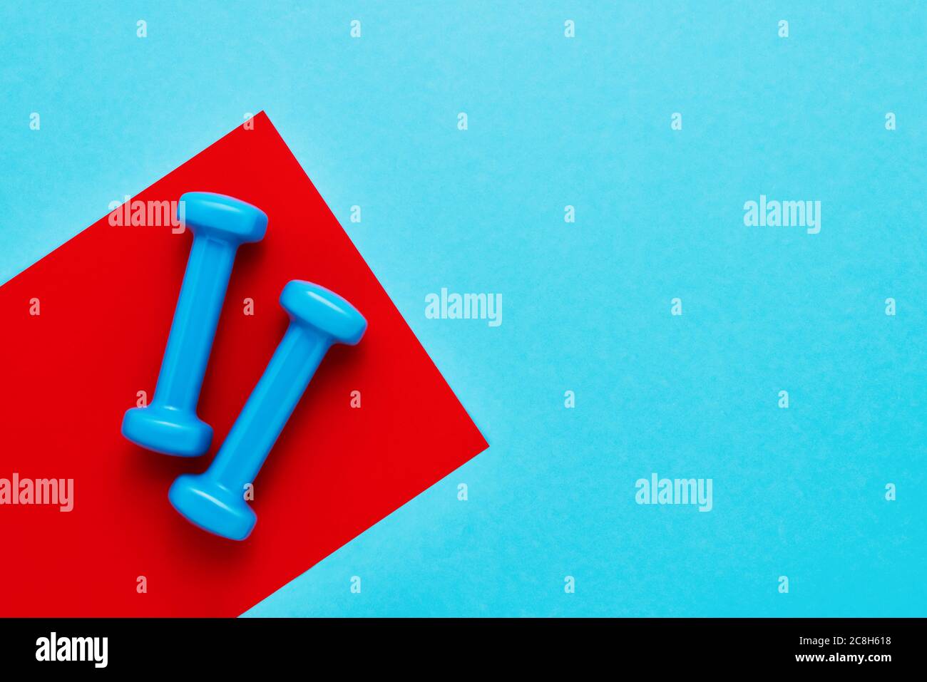 Blaue Kurzhanteln liegen auf rot-blauem Hintergrund. Das Konzept des gesunden Lebensstils. Platz für Text kopieren, Draufsicht Stockfoto