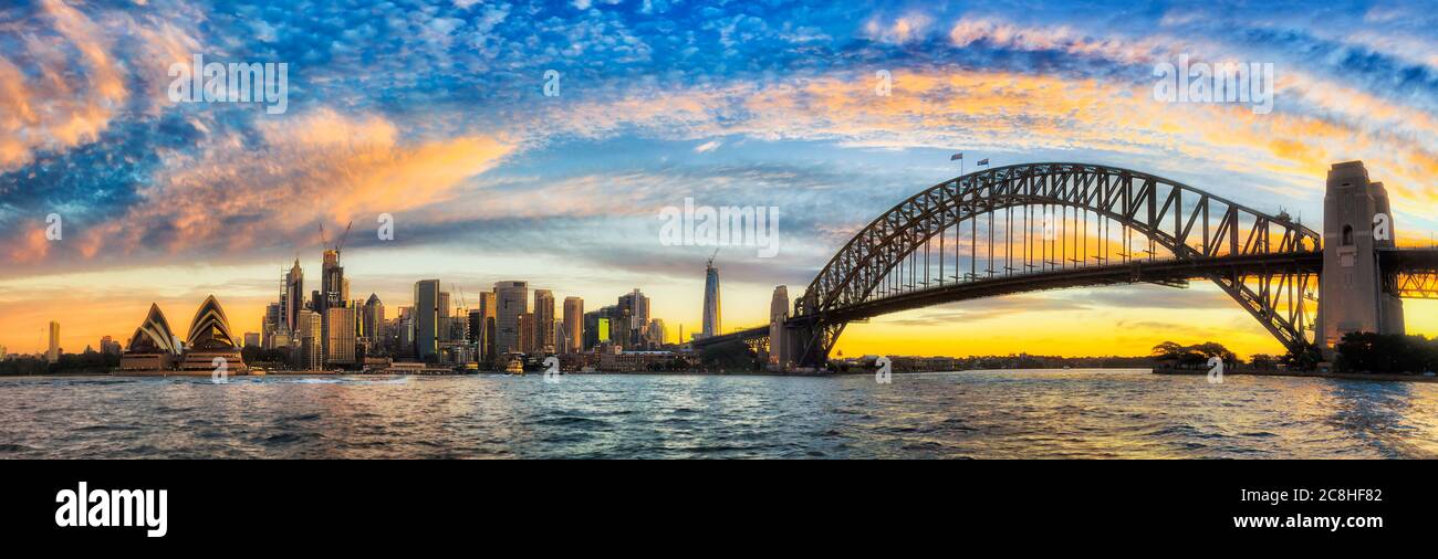Heller Bogen von Sonnenlicht bei Sonnenuntergang über Sydney City CBD Wahrzeichen und Harbour Bridge in weiten Panorama. Stockfoto